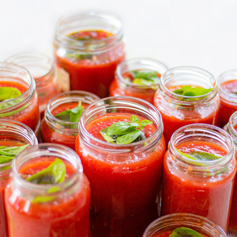 Multiple open mason jars filled with fresh tomato sauce and basil leaves, ready for home canning.