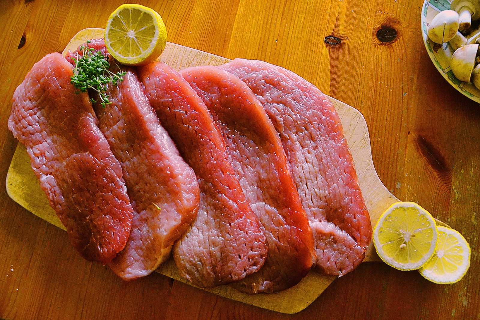 Meat on a cutting board with lemon and herbs.