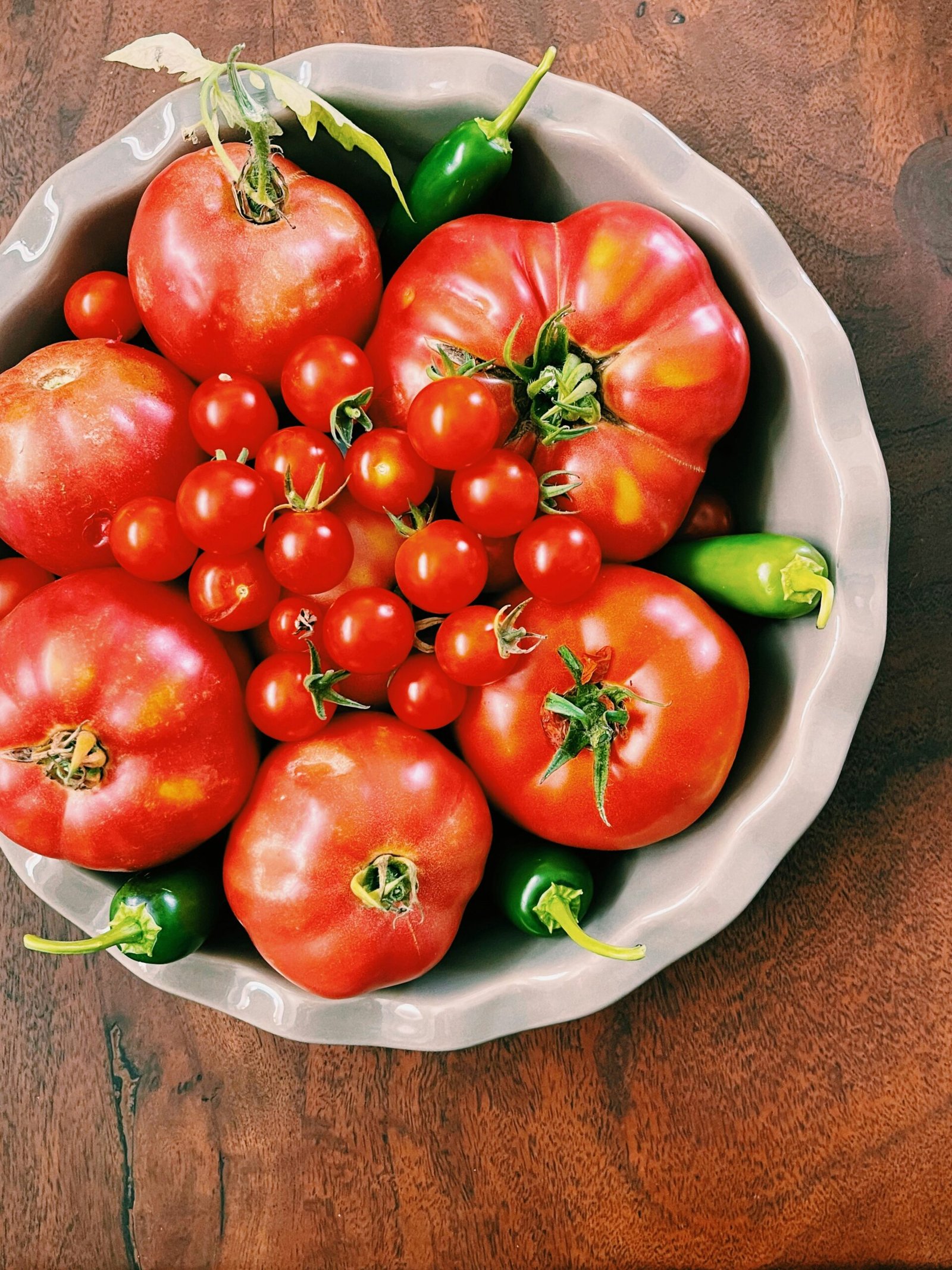 Bowl with fresh tomatoes and peppers sitting on a wooden table