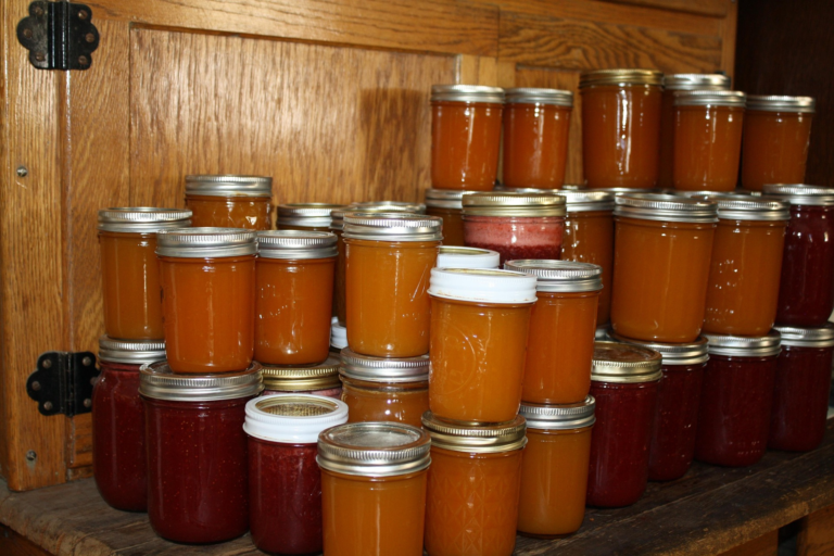 Jars of home canned jam and jelly on wooden shelf.