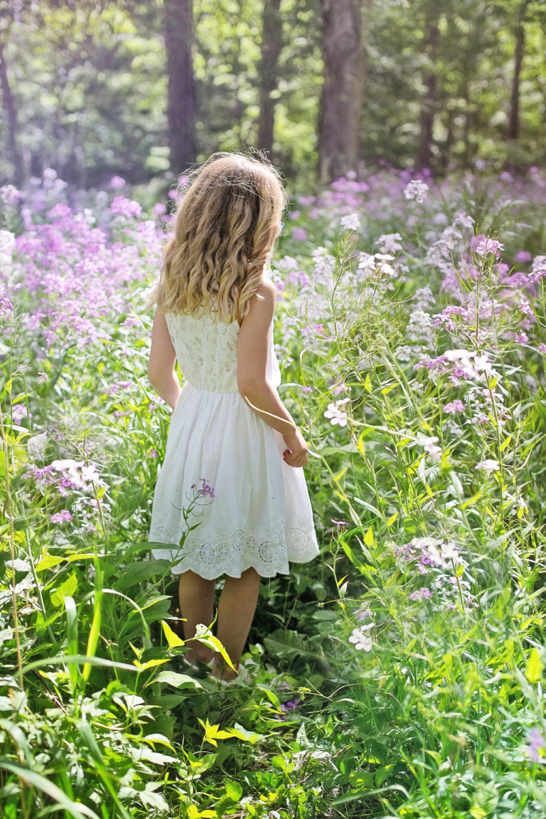 Girl in a white dress walking through a wildflower meadow, seen from behind