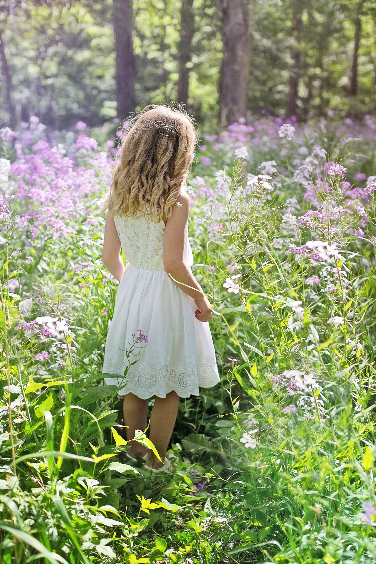 Girl in a white dress walking through a wildflower meadow, seen from behind