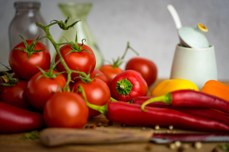 Fresh tomatoes and peppers on a wooden cutting board with a knife to make salsa.